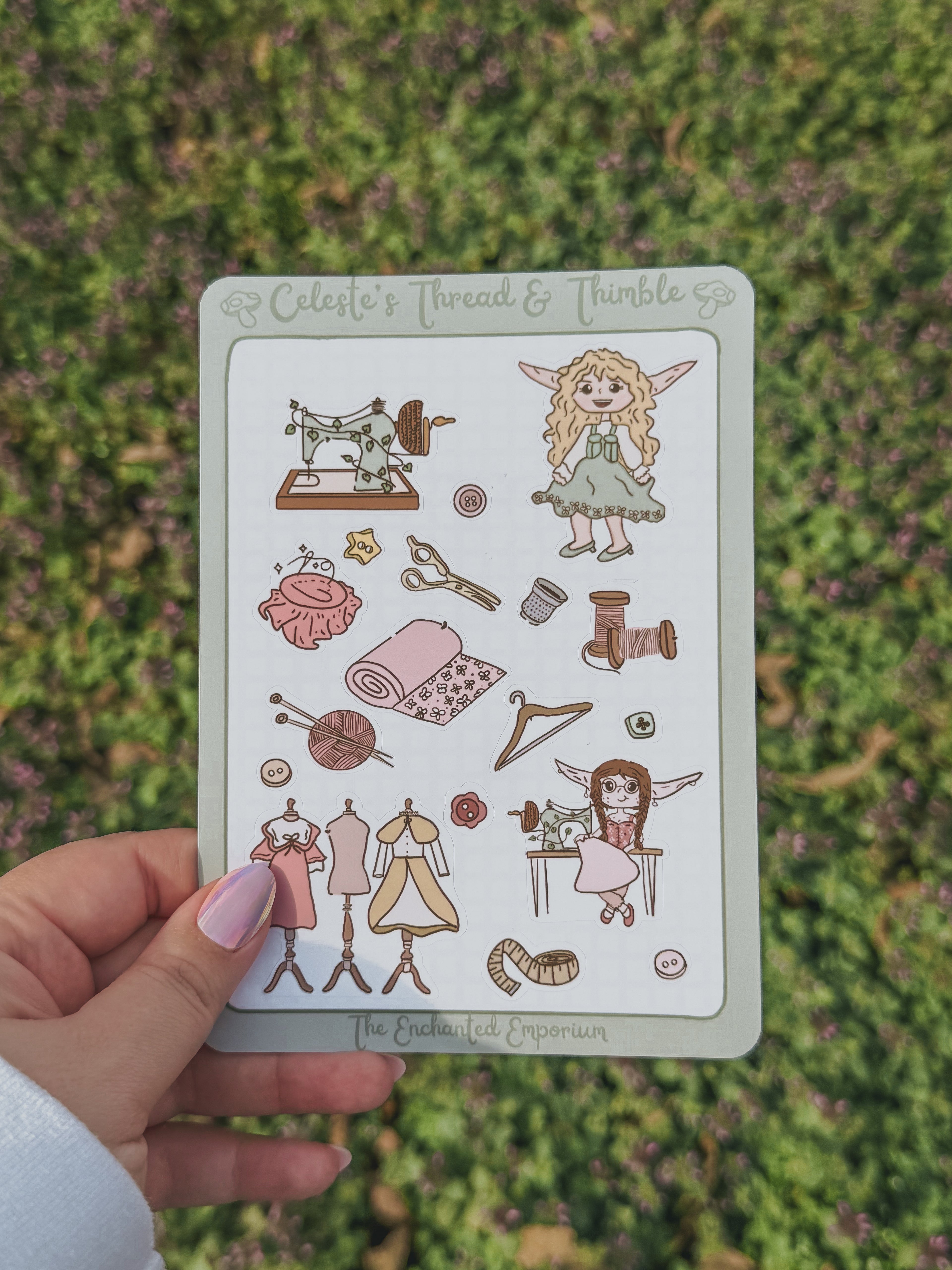 sticker sheet with illustrations of Celeste and sewing-related items held by a hand against a grass background