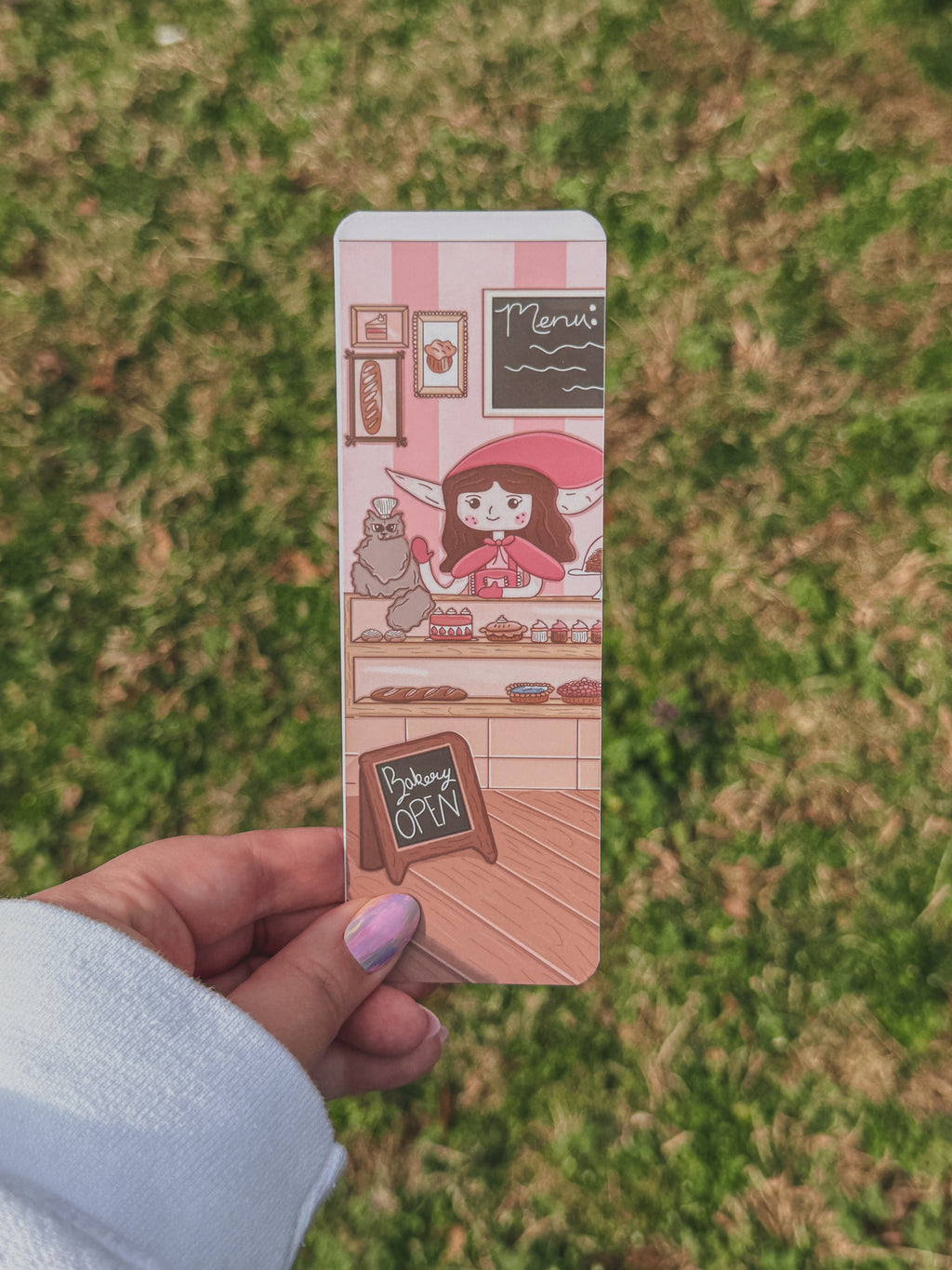 Bookmark with Meadow character held by a hand against a grassy background