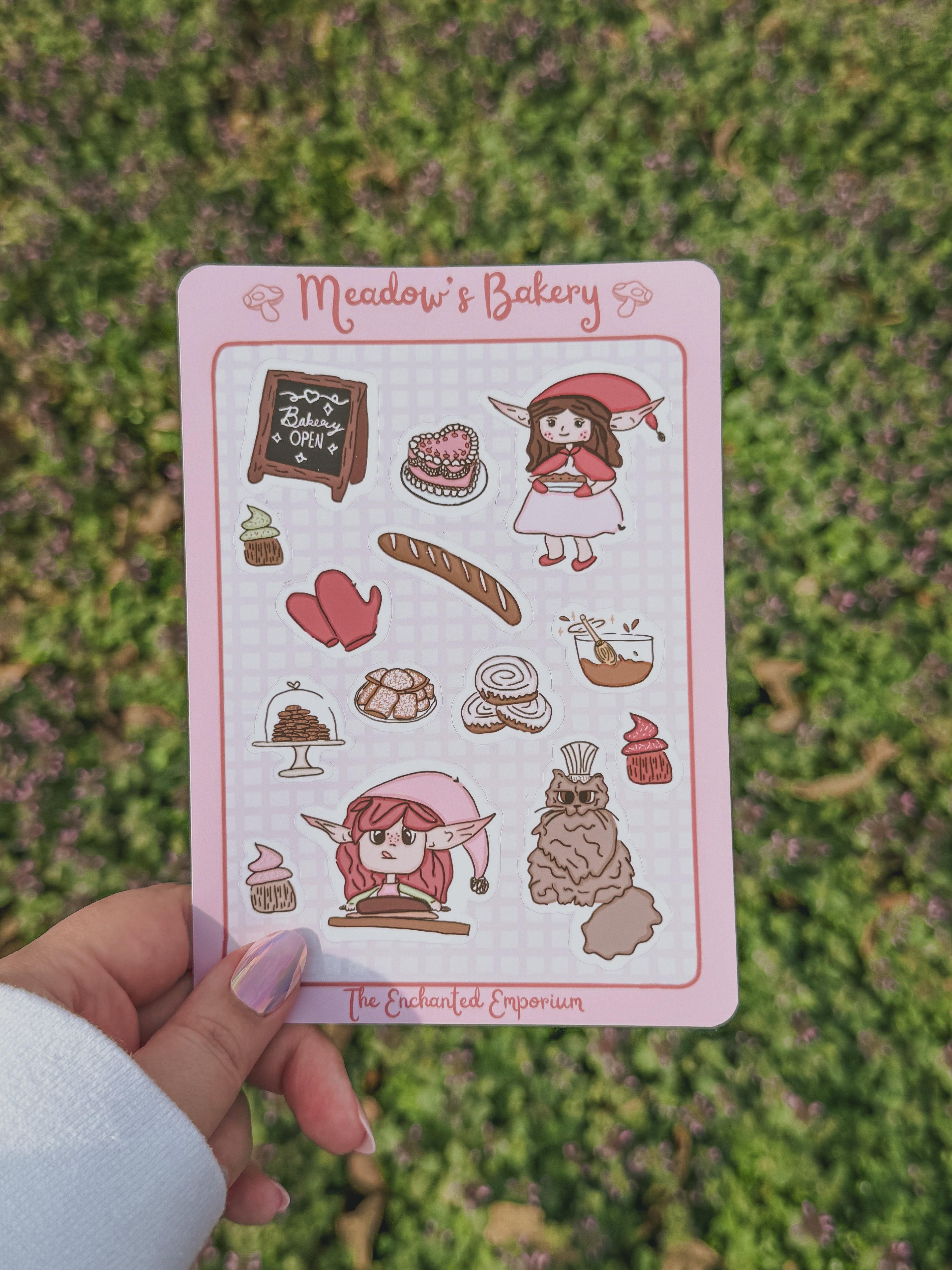 Sticker sheet with illustrations of Meadow and her bakery  held over grass
