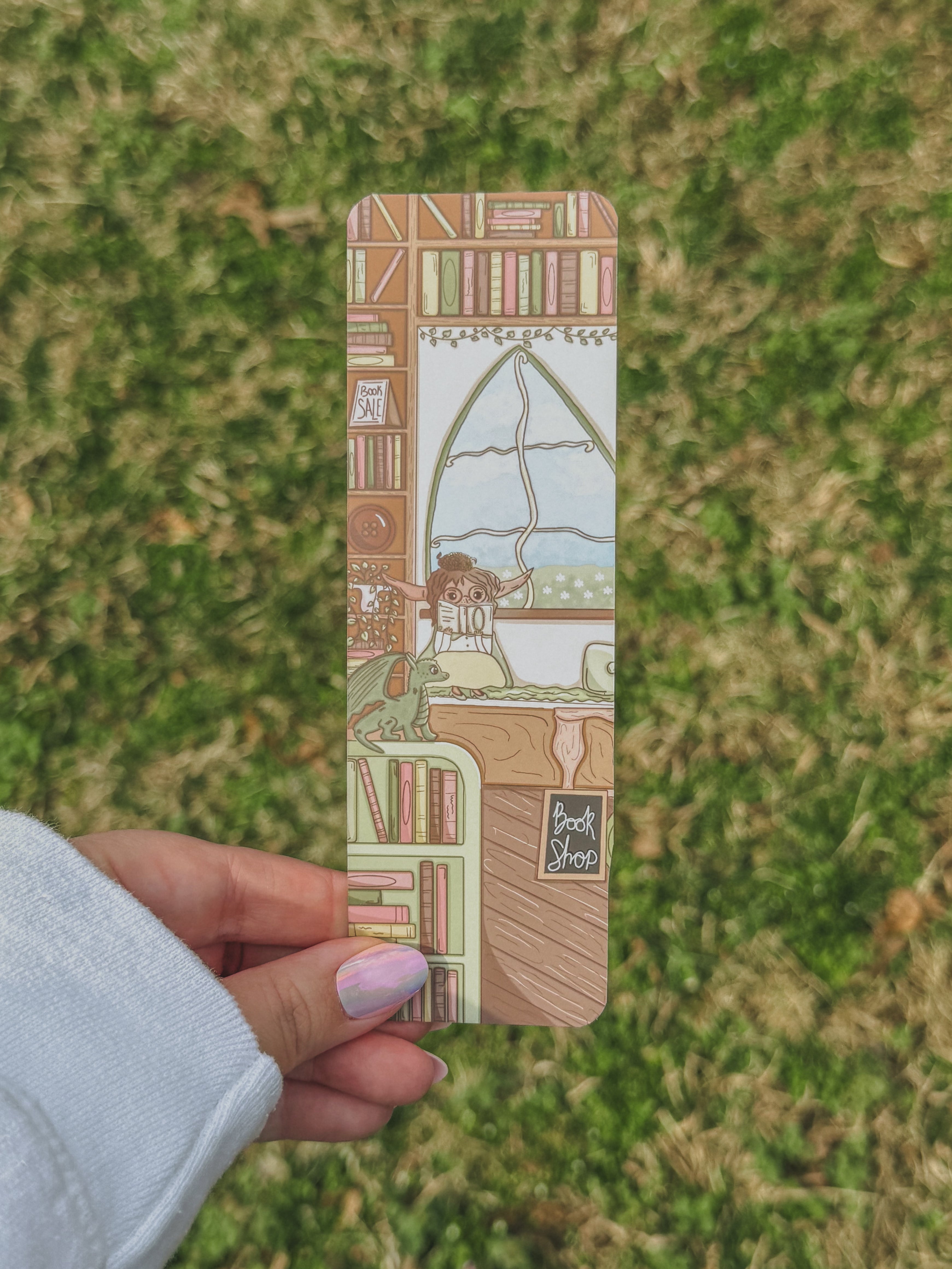 Hand holding a bookmark with a detailed design against a grassy background