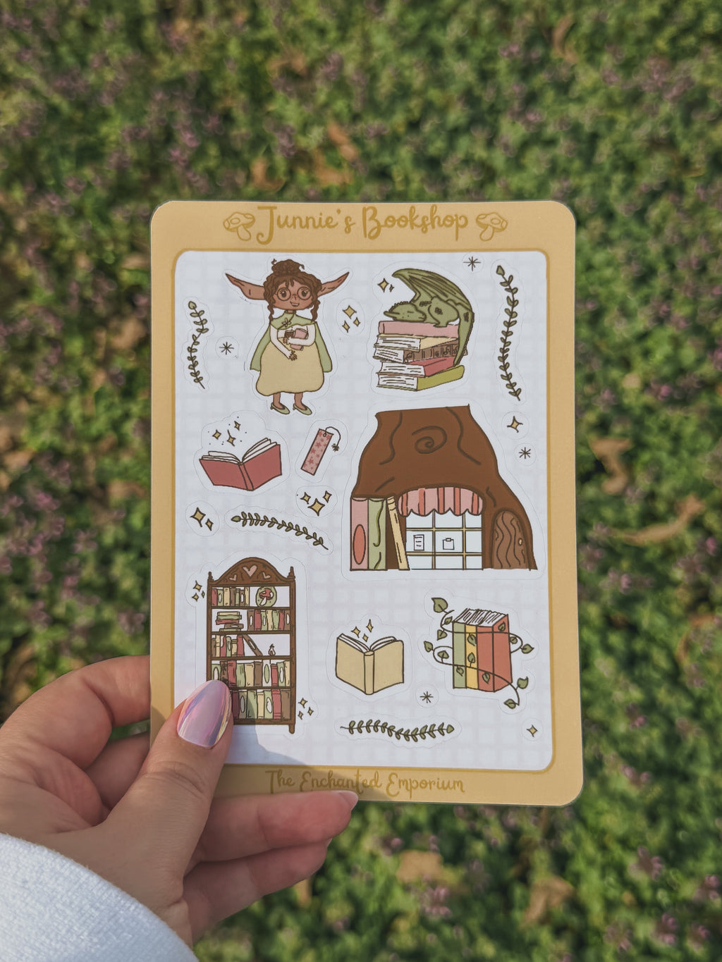 Junnie's sticker sheet illustrations of a bookshop and books held by a hand on a grassy background